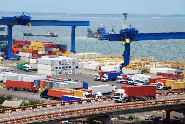 A photograph of a port with shipping containers placed on the dock and freight trucks being loaded